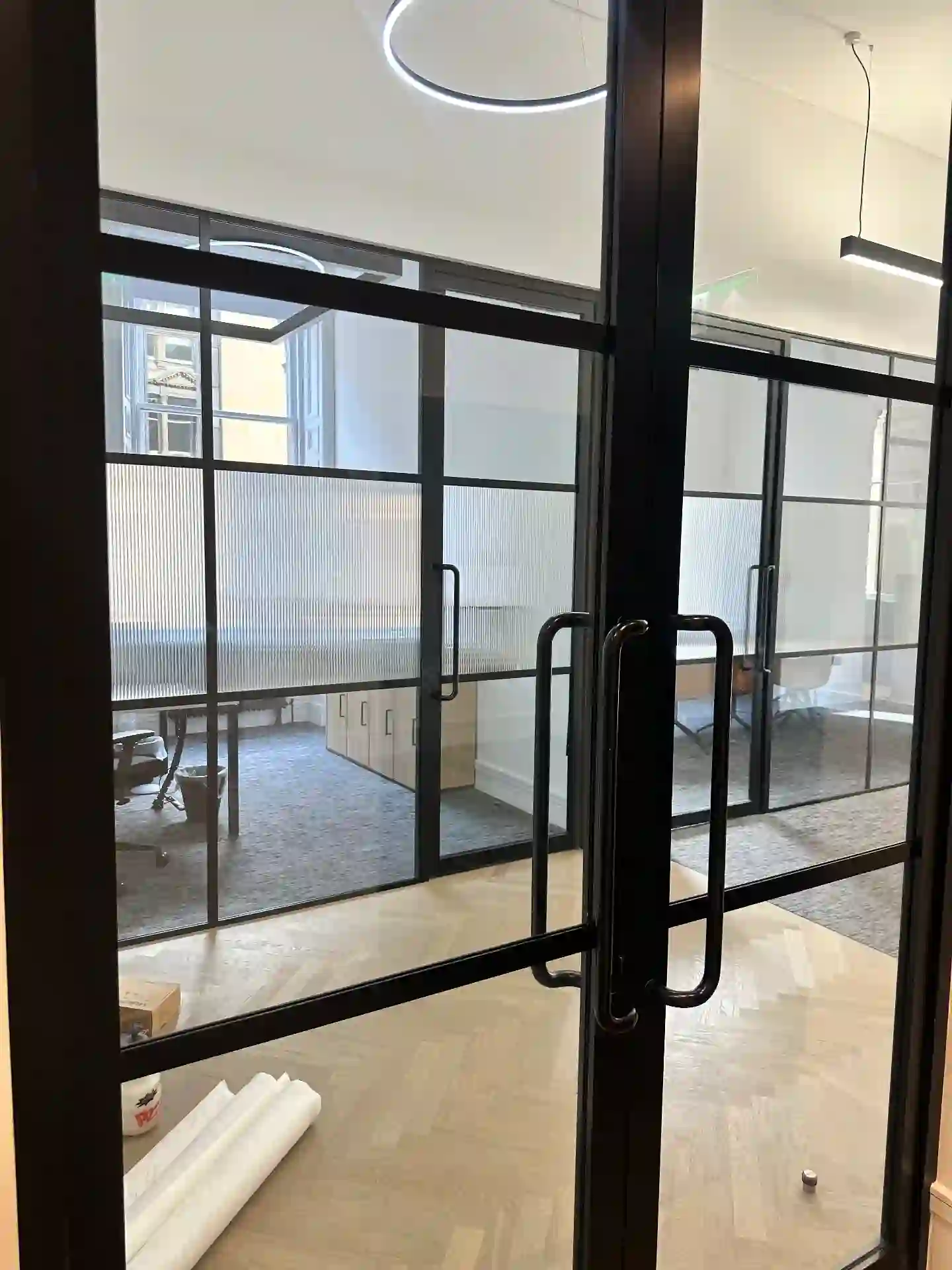 Dark-framed glazed office partitions with a mid-height band of vertical reeded privacy film