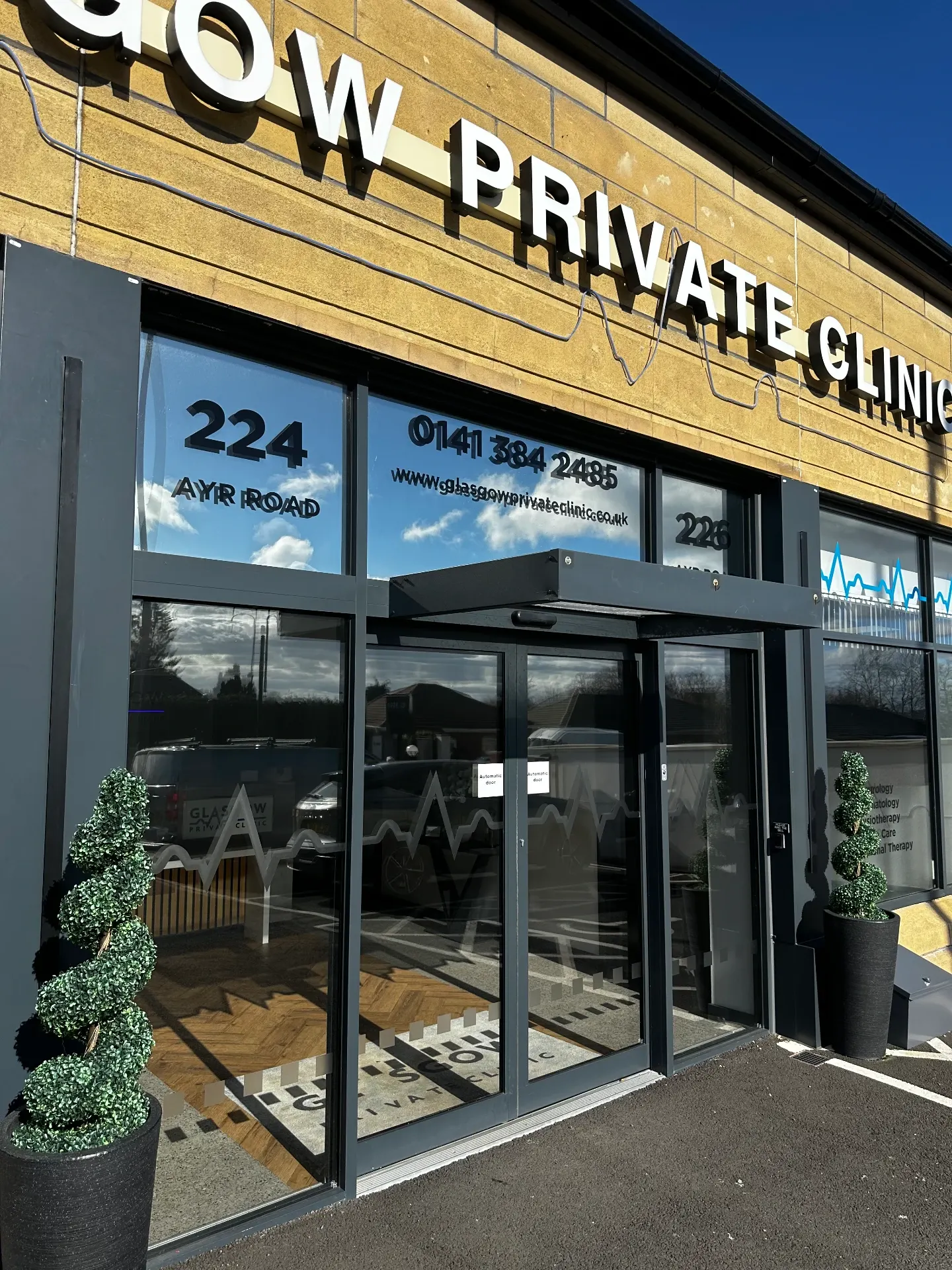Angled view of the Glasgow Private Clinic entrance showing glazed elevation, automatic doors and window graphics