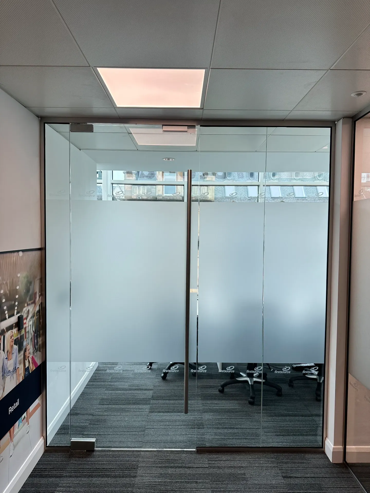 Glass-fronted meeting room with frosted privacy film and logo manifestation bands at head and low level