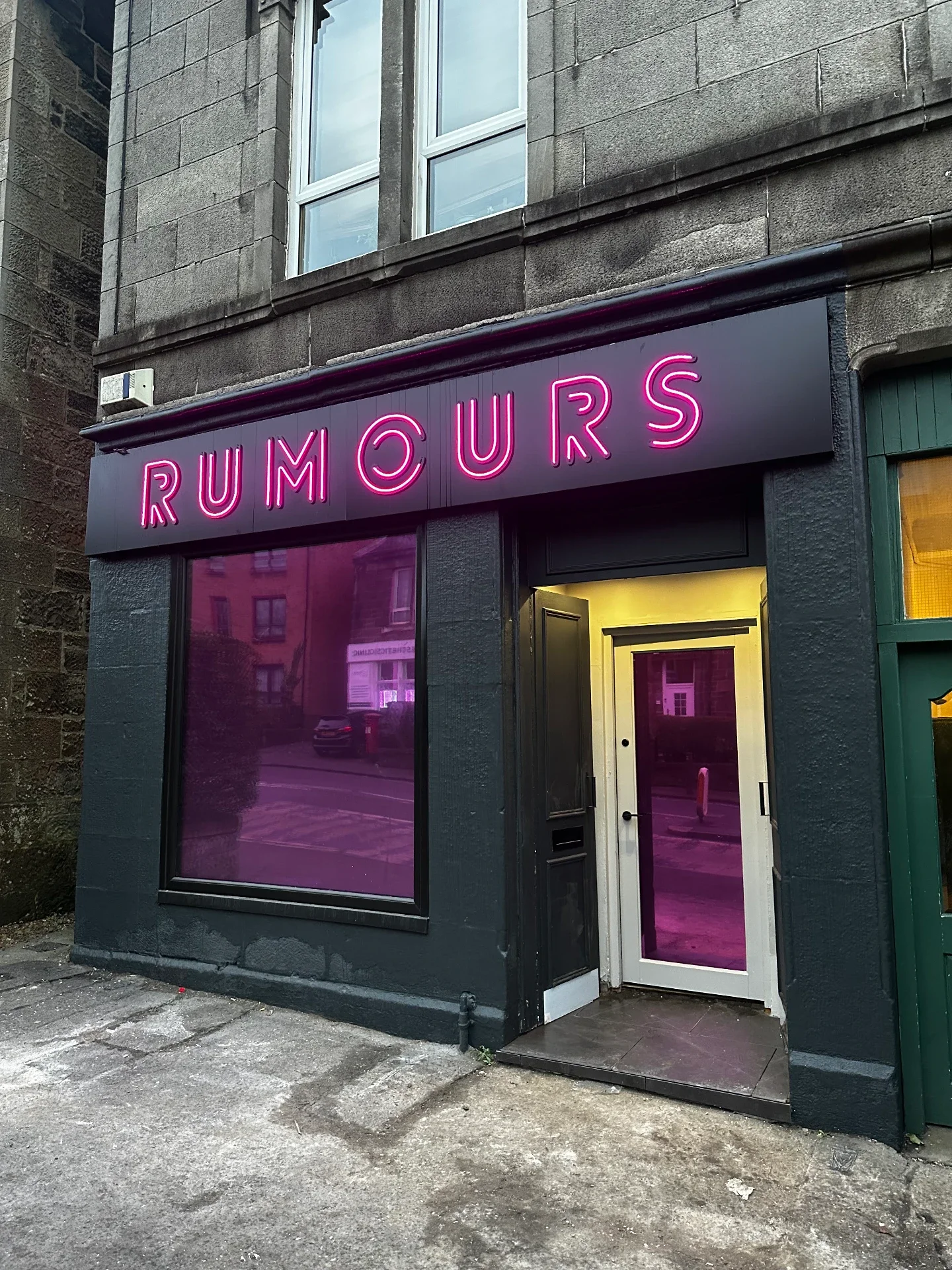 Black fascia with bright pink illuminated neon-effect RUMOURS signage above the pink-tinted shopfront glazing