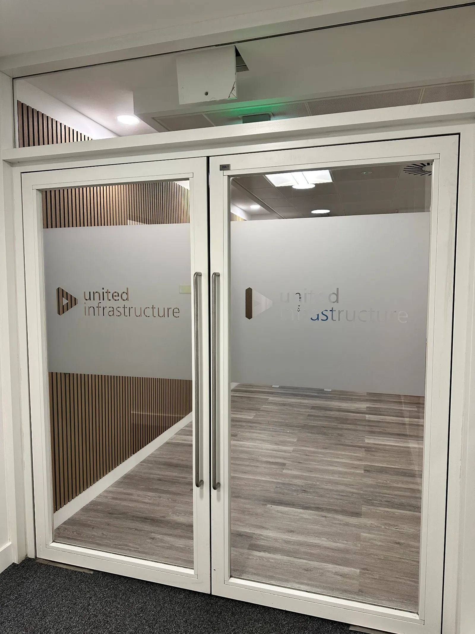 Frosted entrance door panels with cut United Infrastructure logo and wordmark on a Glasgow office floor