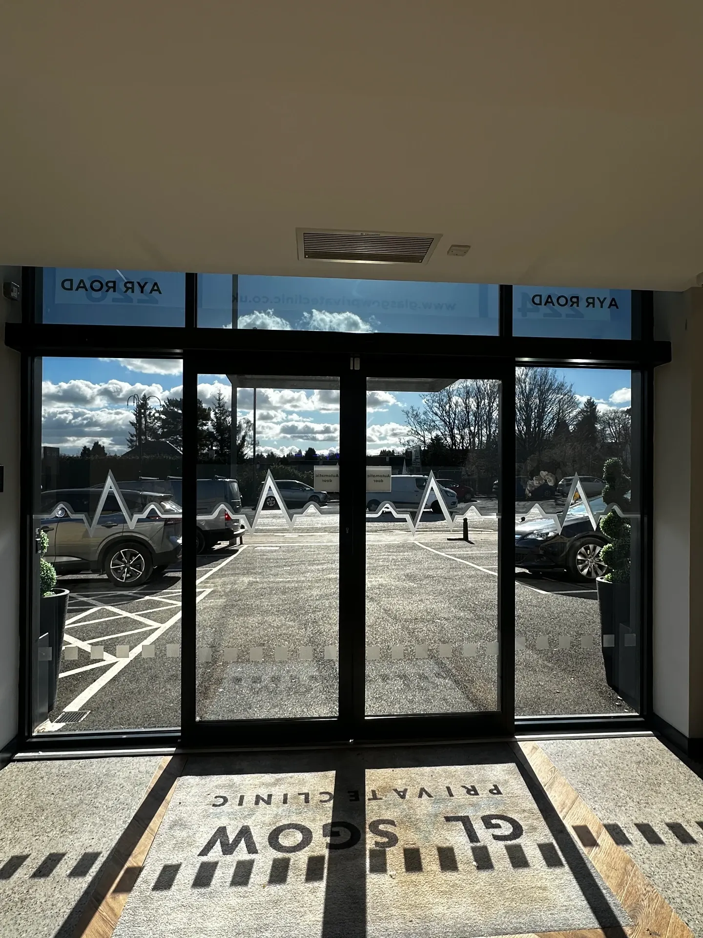 Interior view of the clinic entrance glazing showing reduced glare across the upper glass and the heartbeat manifestation at eye level